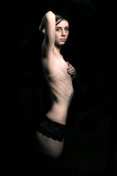 File:Thin Girl in black panties, one hand over her breasts, the other arm raised behind her head.jpg
